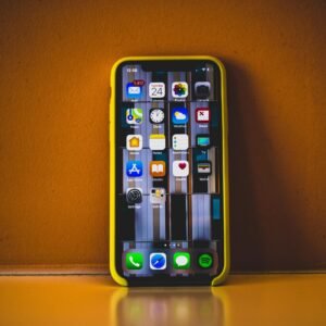Close-up of a smartphone with a yellow case displaying various app icons, reflecting on a surface.